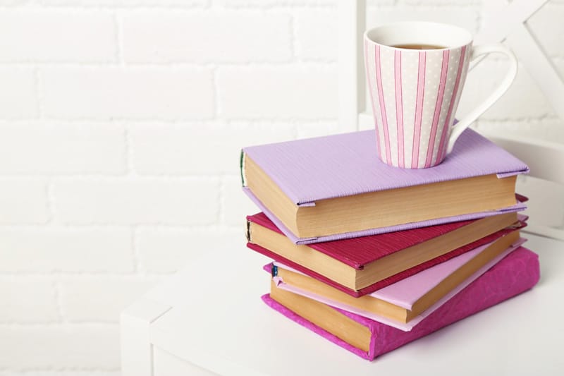 Pile de livres aux couleurs pastel avec une tasse de café, symbolisant la tranquillité d'une librairie virtuelle personnelle pour les auteurs.