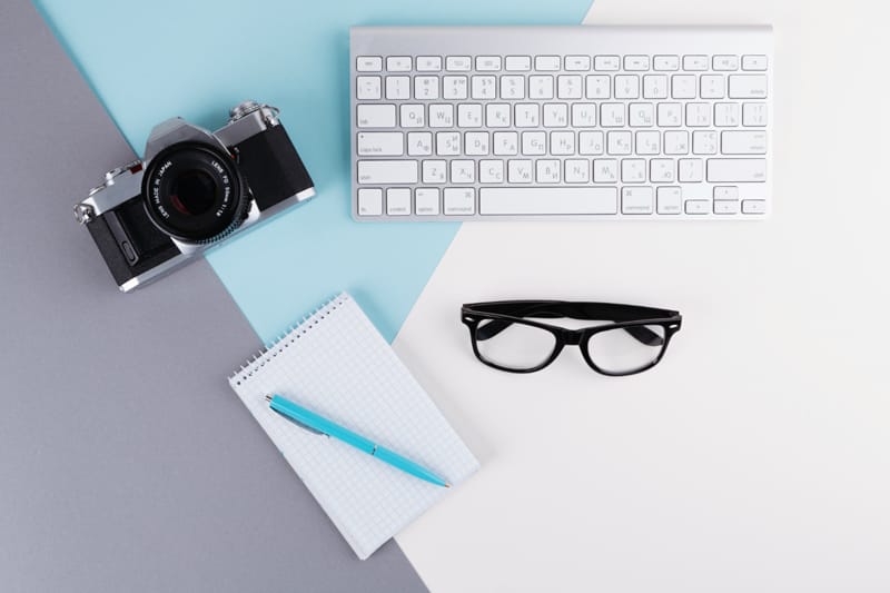 Clavier, appareil photo, carnet et lunettes - Les outils essentiels pour un photographe créant son site web.