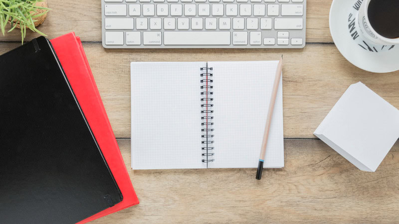 Cahier ouvert avec un clavier, un crayon et des documents pour illustrer l'organisation dans la gestion d'une micro-entreprise.