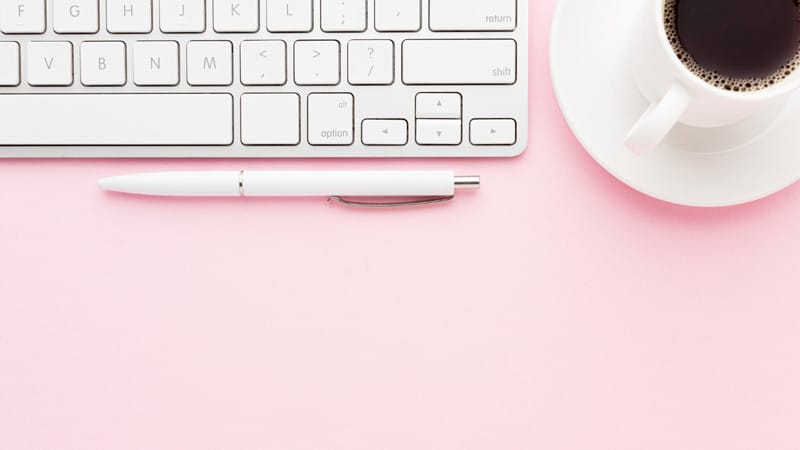 Clavier blanc, stylo et café sur fond rose – Illustration pour un article sur les meilleurs thèmes WordPress gratuits en 2025.