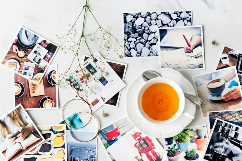 Sélection de photos imprimées sur une table avec une tasse de thé, illustrant le choix d'images pour des projets créatifs.