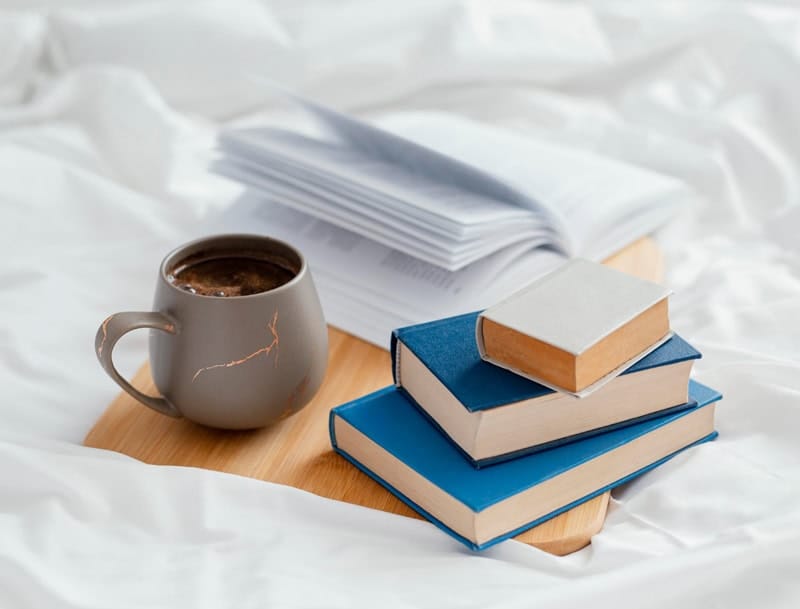 Pile de livres et tasse de café sur un plateau, symbolisant l’univers d’un auteur et son espace de lecture et d’inspiration.